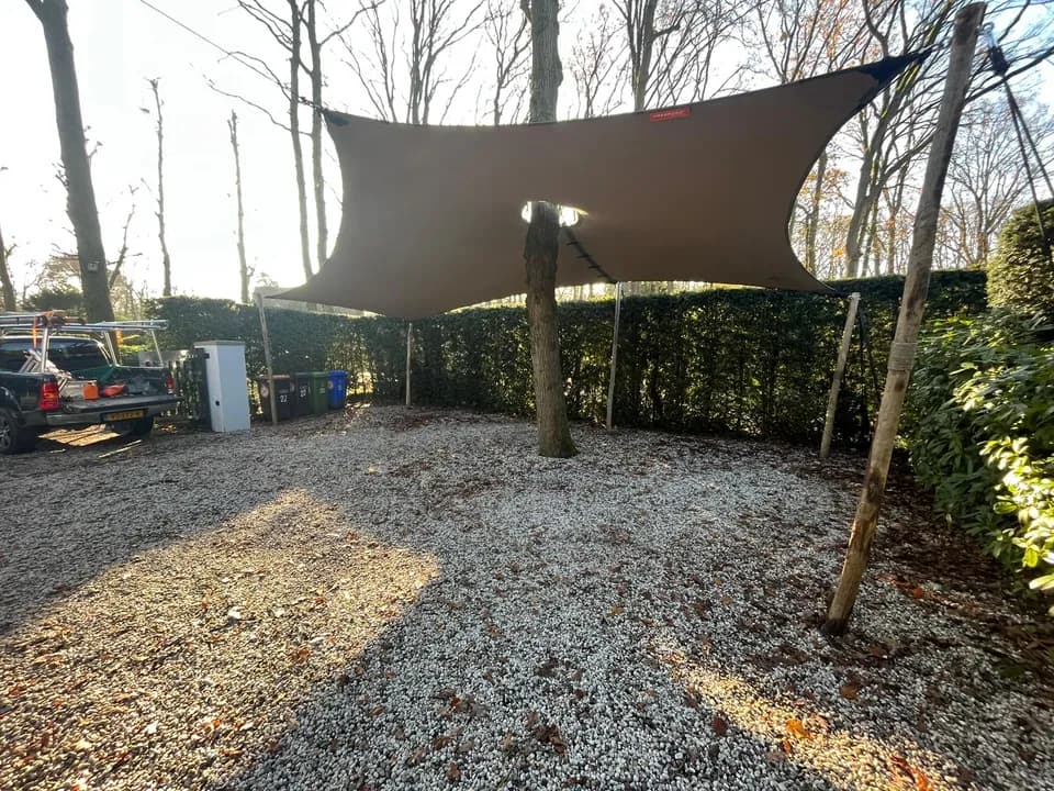 Vrijstaande zandkleurige carport tussen bomen