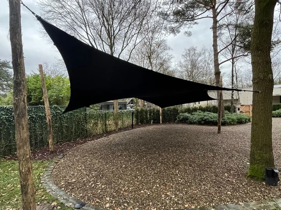 Vrijstaande zwarte carport op een lommerrijke oprit
