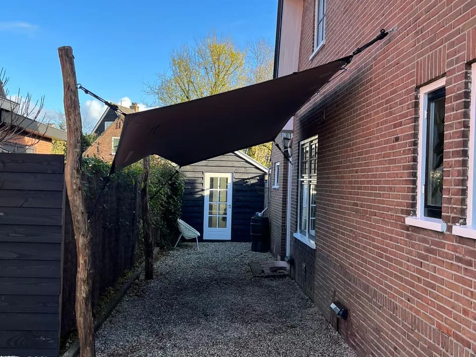 Bruine stretchtent-carport bevestigd naast een woning